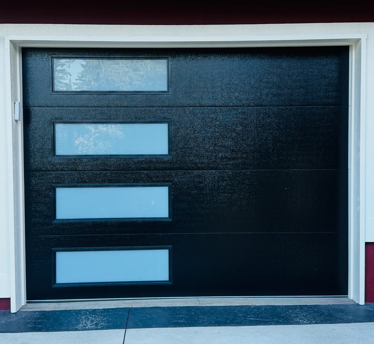Black flush panel garage door with four white laminated glass windows