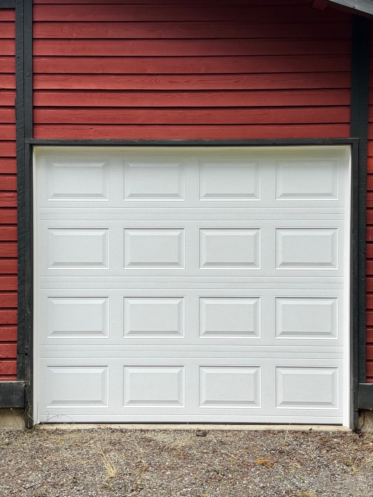 White short raised panel single-car garage door installed on a red wood-sided garage