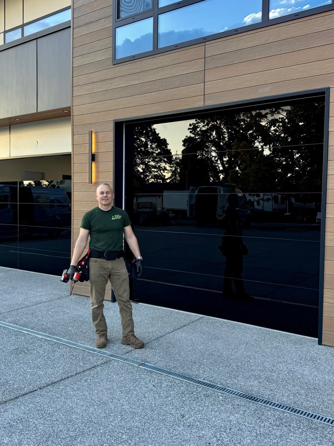 Northwest Garage Doors technician next to a newly installed full-view aluminum garage door at dusk