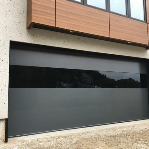 Modern flush garage door in dark grey with a horizontal glass band and wood-paneled upper facade