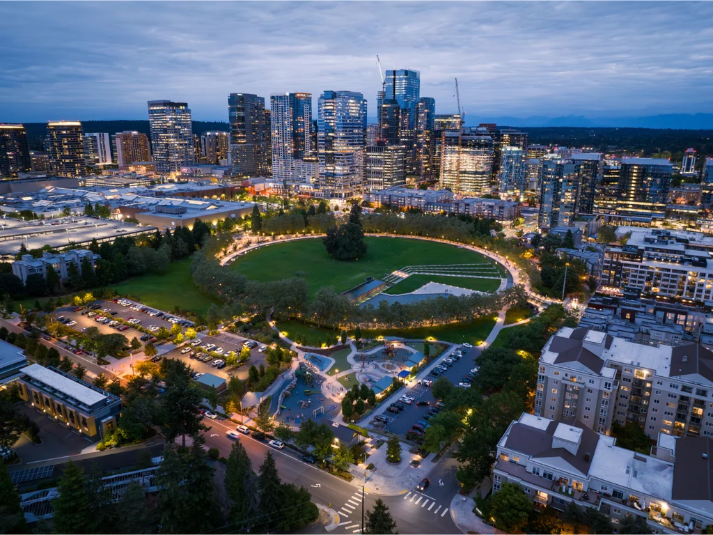 A vibrant cityscape of Bellevue with modern skyscrapers and a lush park, taken at dusk.